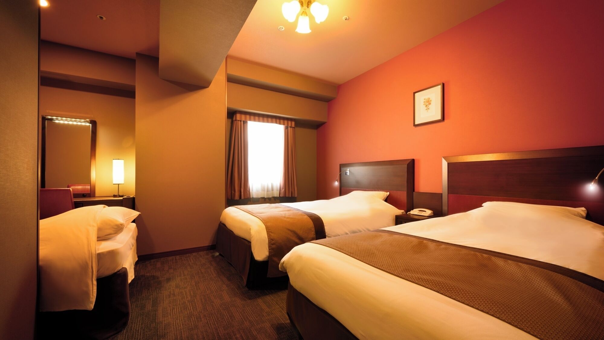 A hotel room with two beds, a bathroom, a mirror, a bedside table with a lamp, and a picture on the wall.