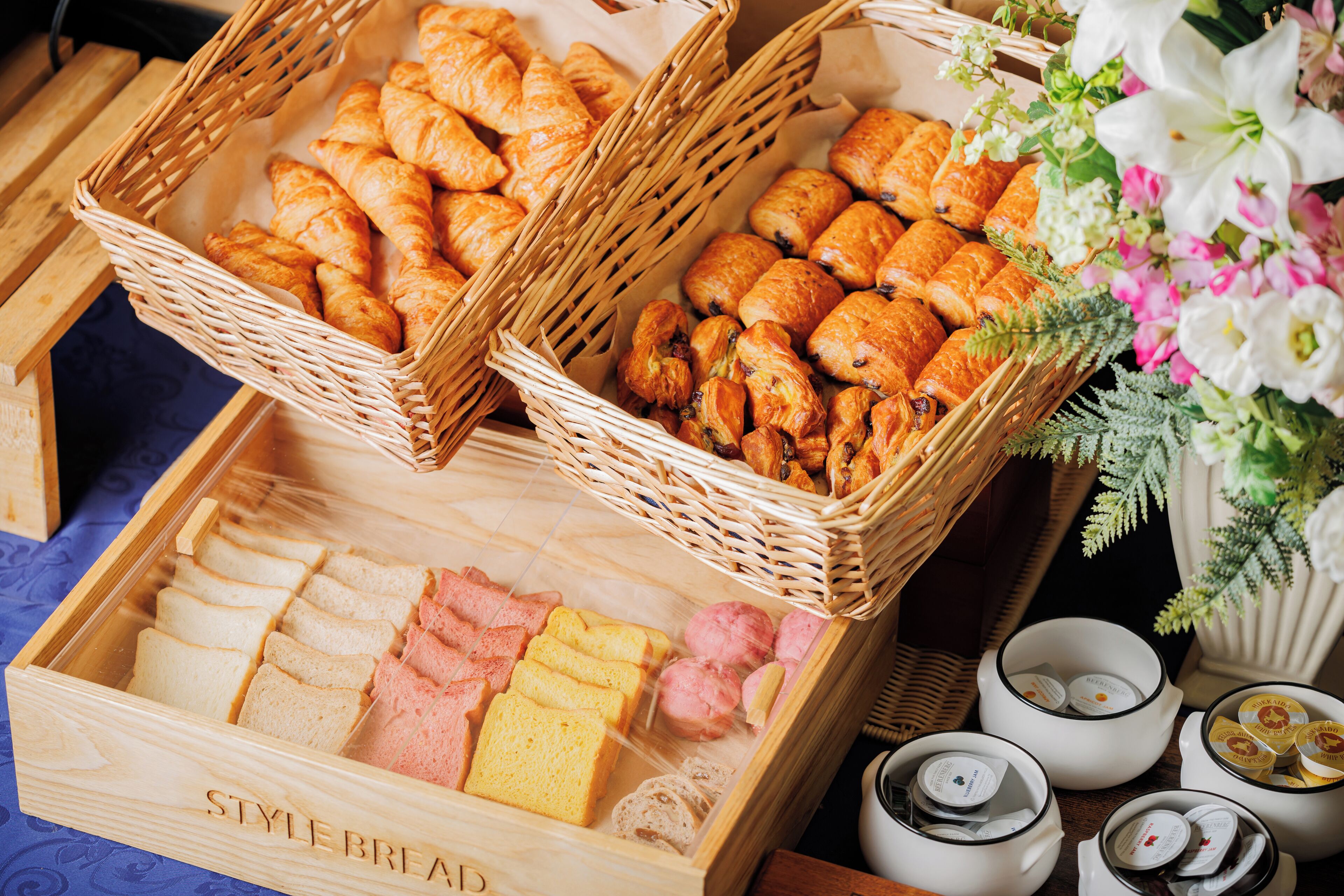 A variety of pastries and bread in wicker baskets and wooden boxes, with small containers of condiments on the side.