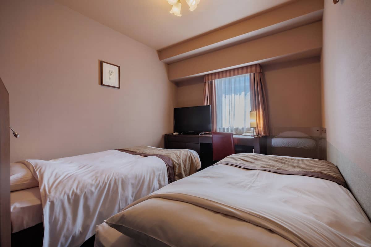 A hotel room with two beds, a desk, a television, and a window with curtains.