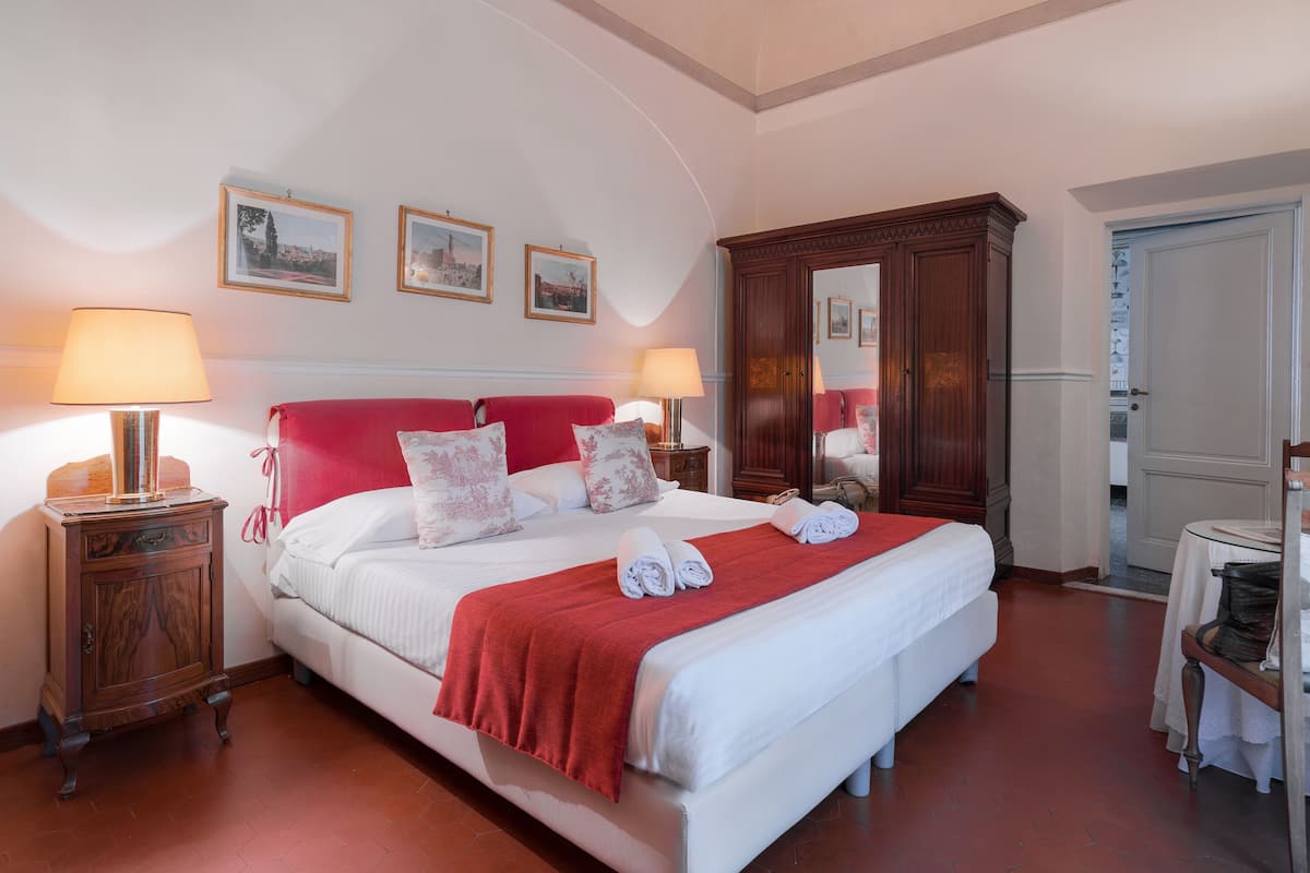 Una cama bien hecha con un edredón rojo, dos lámparas de noche y un armario de madera en una habitación de hotel.
