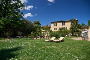 Eine Villa mit Garten, zwei Liegestühlen und blauem Himmel.