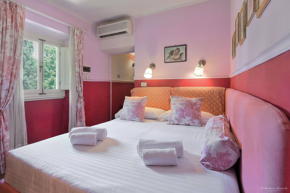 A hotel room with a bed, pillows, and a window with curtains.