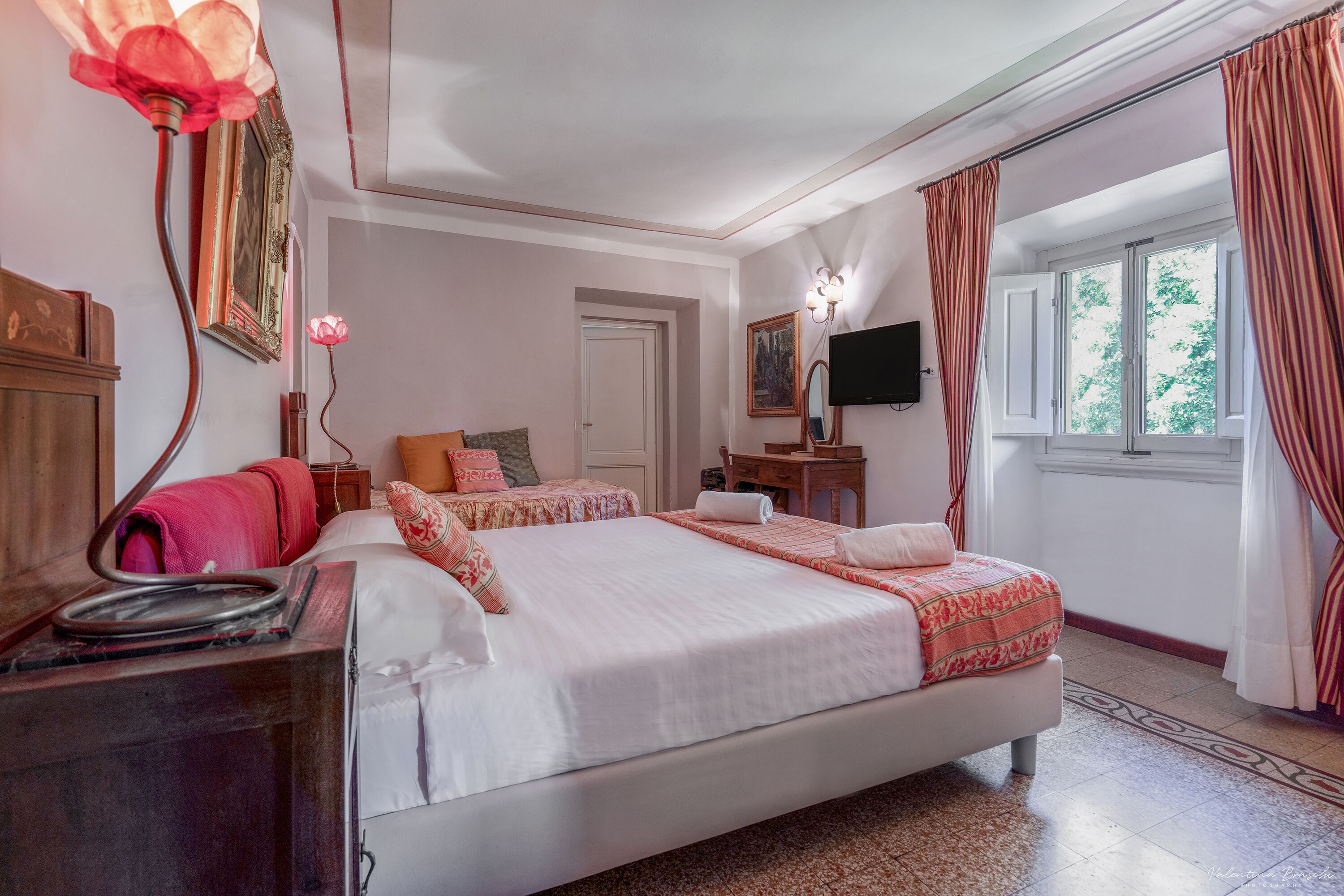 Une chambre d’hôtel avec un grand lit, un bureau avec un téléphone, une télévision et une fenêtre avec des rideaux.