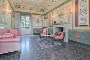 A room with a marble floor, a pink sofa, a small round table, and chairs with pink cushions.