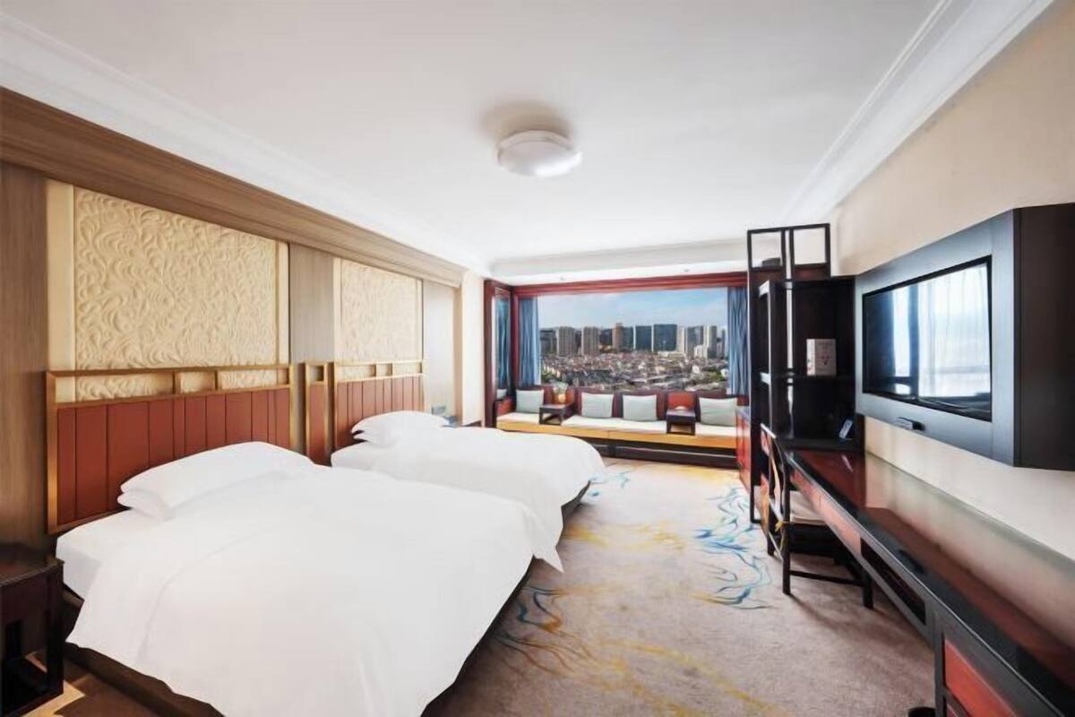 Een hotelkamer met twee bedden, een grote televisie en uitzicht over de stad.