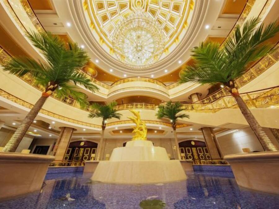 A grand lobby with a central fountain, palm trees, and a decorative ceiling.