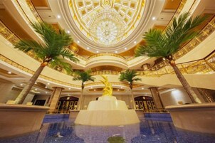 A grand lobby with a central fountain, palm trees, and a decorative ceiling.