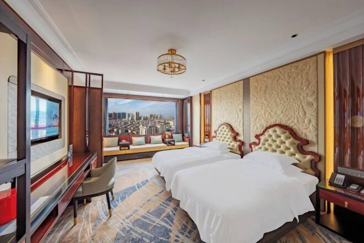 Een hotelkamer met twee bedden, een televisie, uitzicht over de stad en een kroonluchter.
