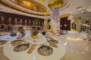 Un lobby de hotel lujoso con una mesa redonda central dispuesta para comer, un pilar decorativo grande y una zona de recepción con mostrador y asientos.