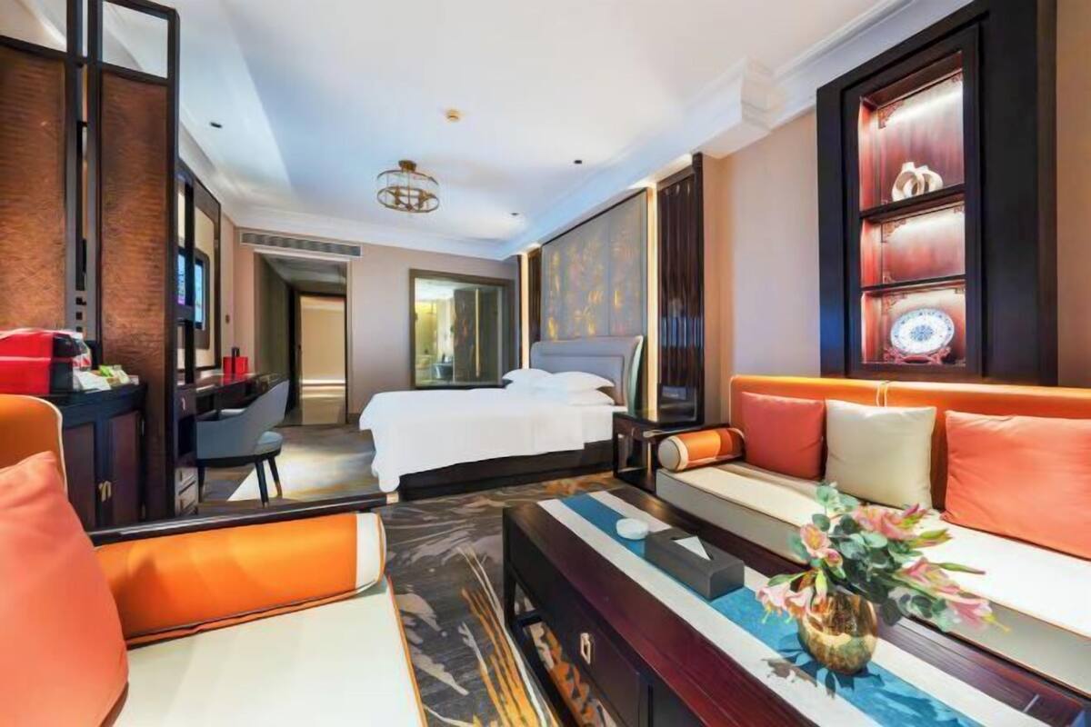 Een hotelkamer met een bed, bank, televisie en een decoratieve vaas.