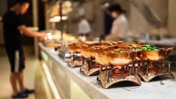 A buffet line with various dishes in metal serving dishes, a person serving food, and a counter with a menu.