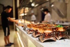 A buffet line with various dishes in metal serving dishes, a person serving food, and a counter with a menu.