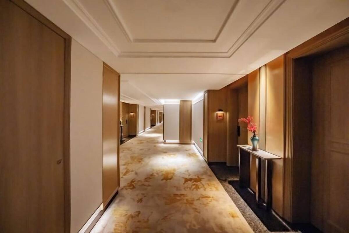 Een hotelgang met houten deuren, een kamerbreed tapijt met dessin en een kleine tafel met een bloevas.