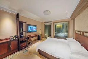 A hotel room with a large bed, a desk with a computer, a television, and a glass door leading to a bathroom. - Haitian Hotel (Jinhua)