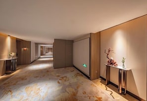 A hotel corridor with a patterned carpet, a reception desk, and a wall-mounted exit sign. - Haitian Hotel (Jinhua)