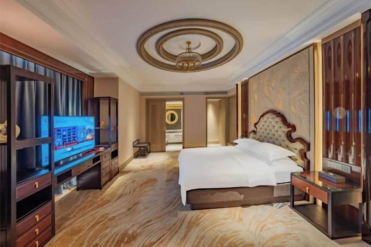 Een hotelkamer met een groot bed, een televisie, een houten kast en een kroonluchter.