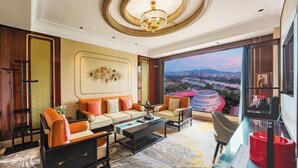 Una habitación de hotel moderna con un ventanal grande, una araña, un conjunto de sofás y una mesa de centro.