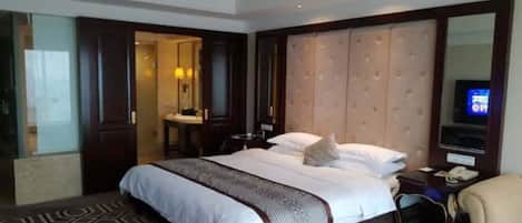 A hotel room with a large bed, a bedside table, a chair, a mirror, and a TV.