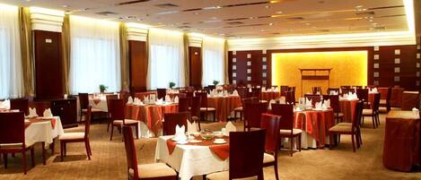 Un amplio salón de banquetes con varias mesas redondas dispuestas para comer, cada una con mantel blanco y servilletas rojas.