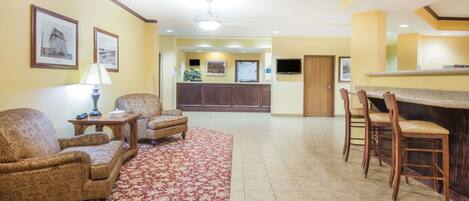 Un hall de hotel con mostrador de recepción, dos sofás, una mesa de centro y una zona de bar con sillas.