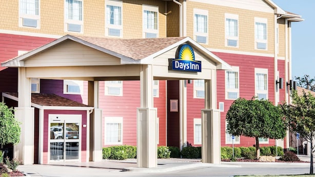 A Days Inn hotel with a red and beige exterior, a covered entrance, and a clear sky. - Days Inn by Wyndham Ellis (Ellis)