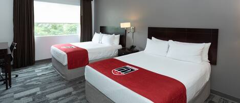 A hotel room with two beds, a desk, and a window with curtains.