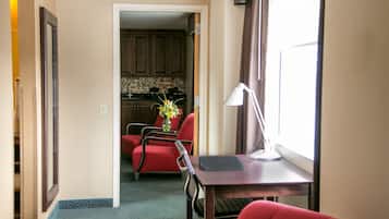 A hotel room with a desk, chair, and a view of the kitchen.