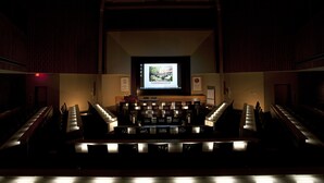 An auditorium with tiered seating, a central stage, and a large screen displaying 'THE GEORGIA CENTER'. - The University of Georgia Center for Continuing Education & Hotel (Athens)