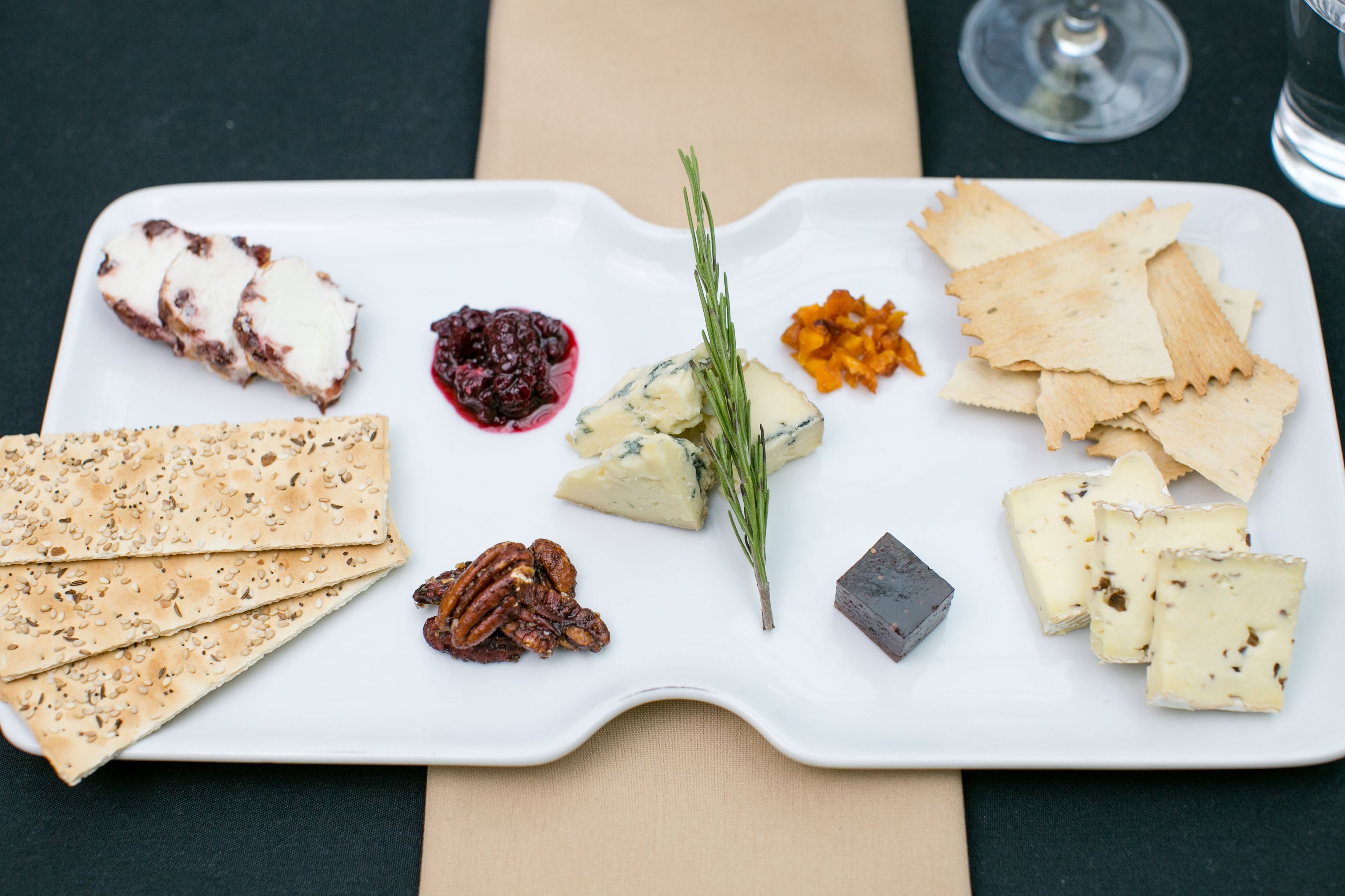 A white rectangular plate with various cheeses, crackers, and nuts.