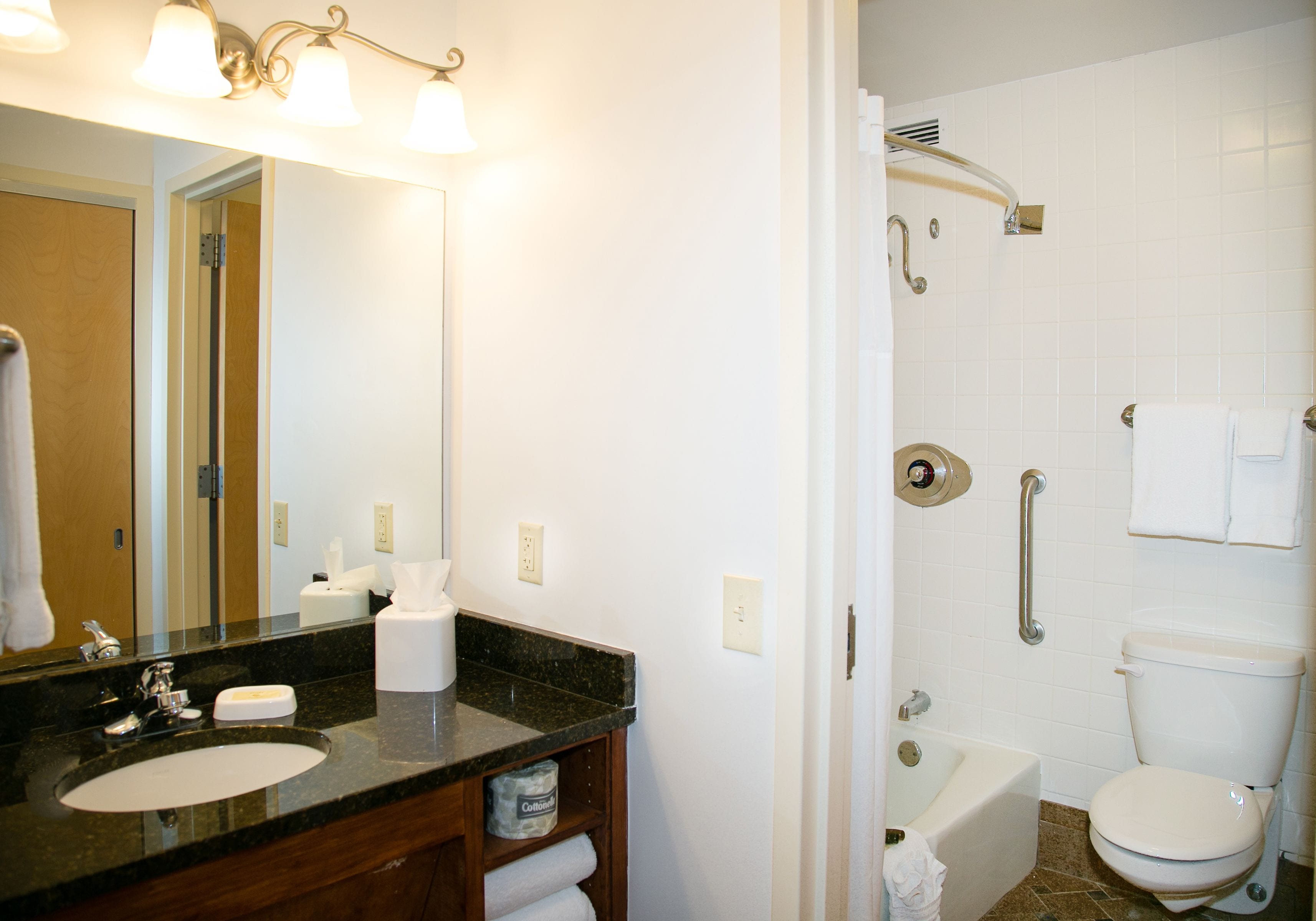 A bathroom with a sink, mirror, towel rack, and shower with a grab bar.