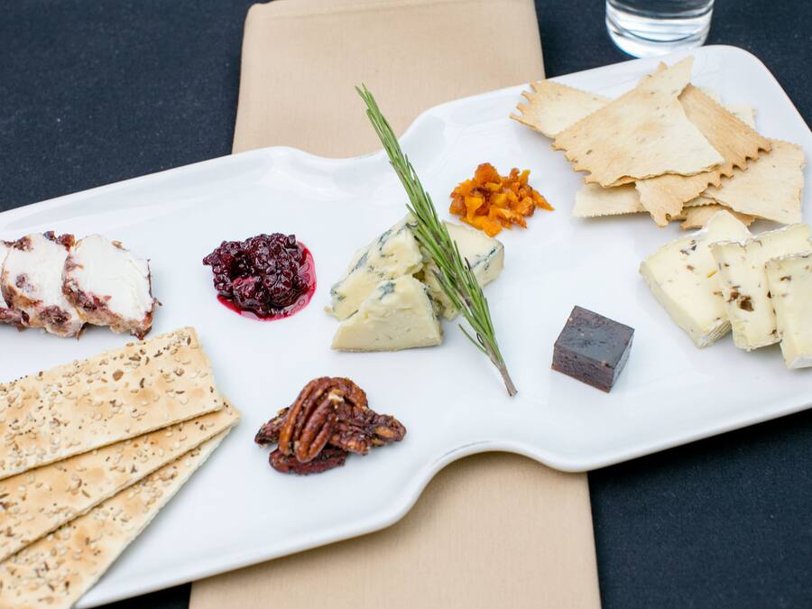 Un plato rectangular blanco con varios quesos, galletas y una ramita de romero.