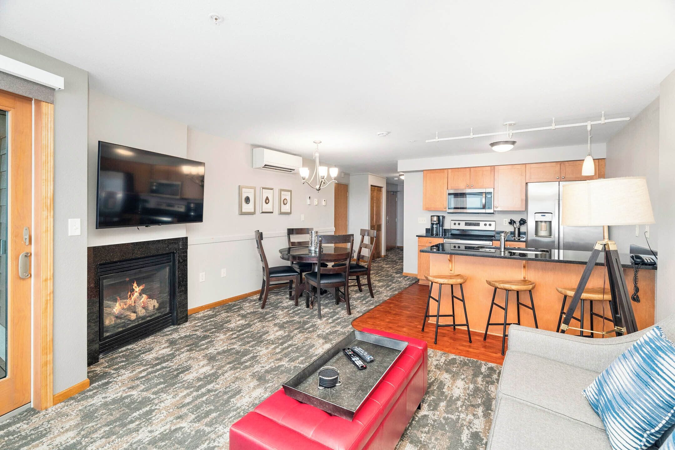 A modern living room with a fireplace, a TV, and a kitchen area with bar stools.