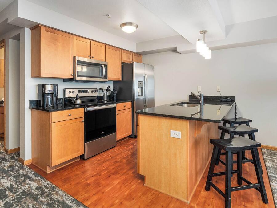 A modern kitchen with wooden cabinets, stainless steel appliances, and a central island with stools.