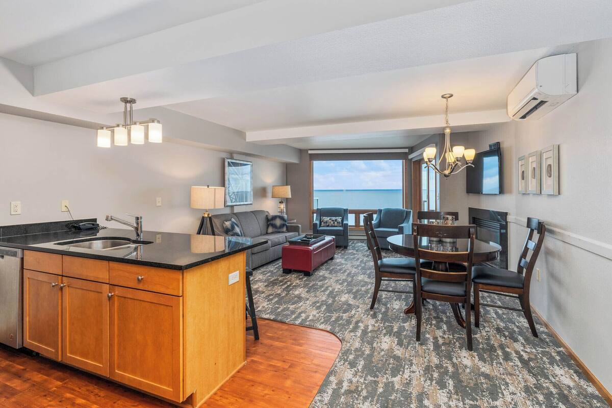 A modern kitchen with a central island, a dining area with a round table and chairs, and a view of the ocean.