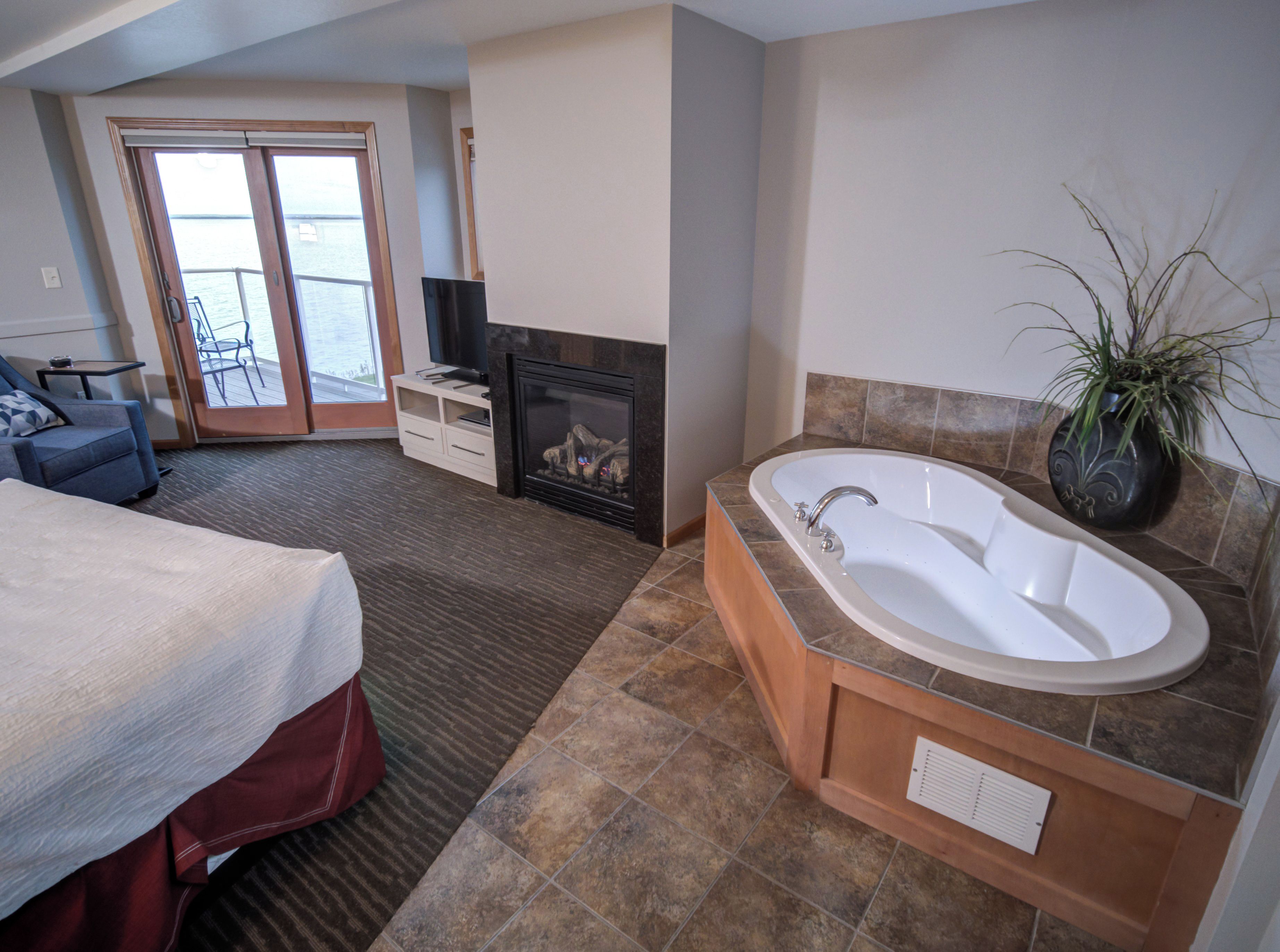 Habitación de hotel con una cama grande, chimenea, bañera y vista al mar a través de una puerta corrediza.
