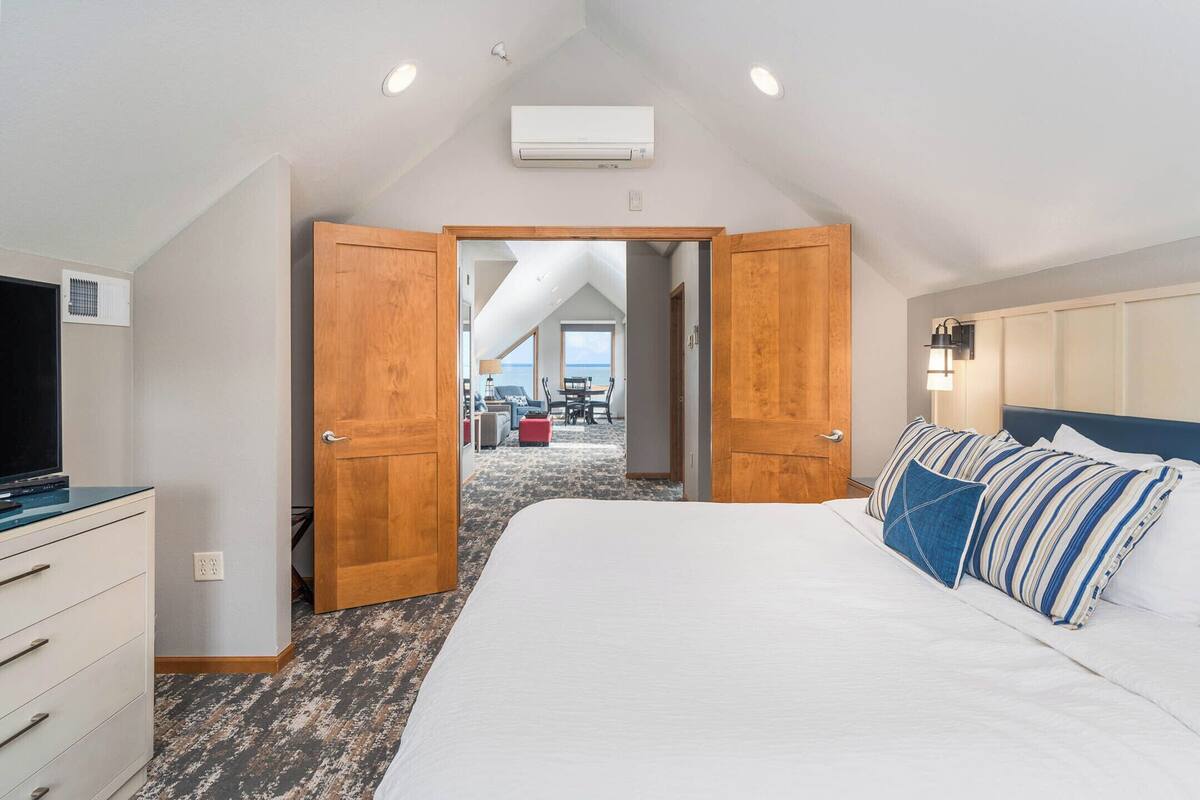 A bedroom with a large bed, wooden doors, a TV, and an air conditioning unit.