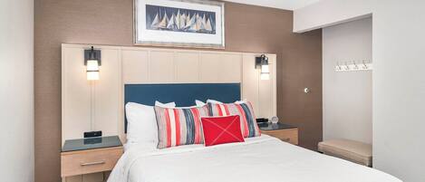 A hotel room with a large bed, two bedside tables, a nightstand, a framed picture on the wall, and a bench by the door.