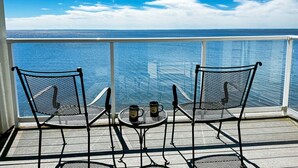 A balcony with two chairs and a small table, overlooking a body of water.