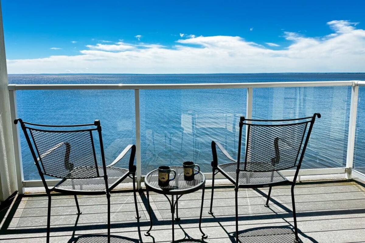 A balcony with two chairs and a small table, overlooking a body of water.