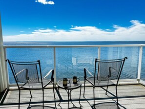 A balcony with two chairs and a small table, overlooking a body of water.