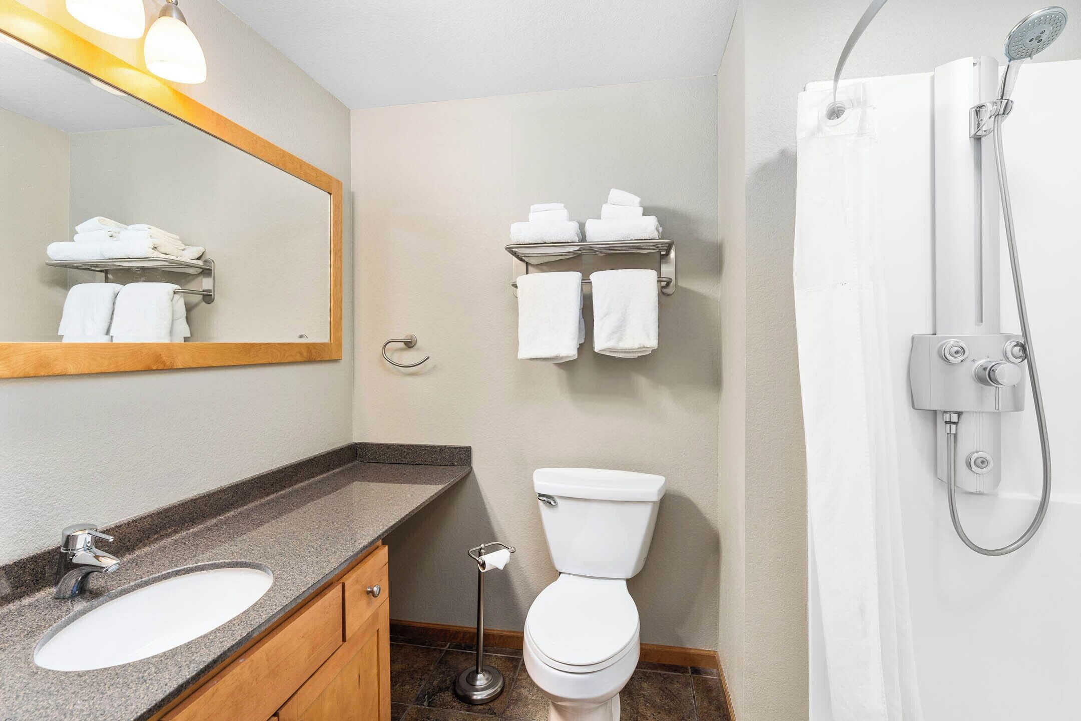 A bathroom with a sink, toilet, and shower. There are towels on a rack and a mirror above the sink.