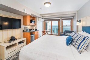 A hotel room with a large bed, a TV, a kitchenette, and a balcony with a view of the ocean. - Beacon Pointe on Lake Superior (Duluth)