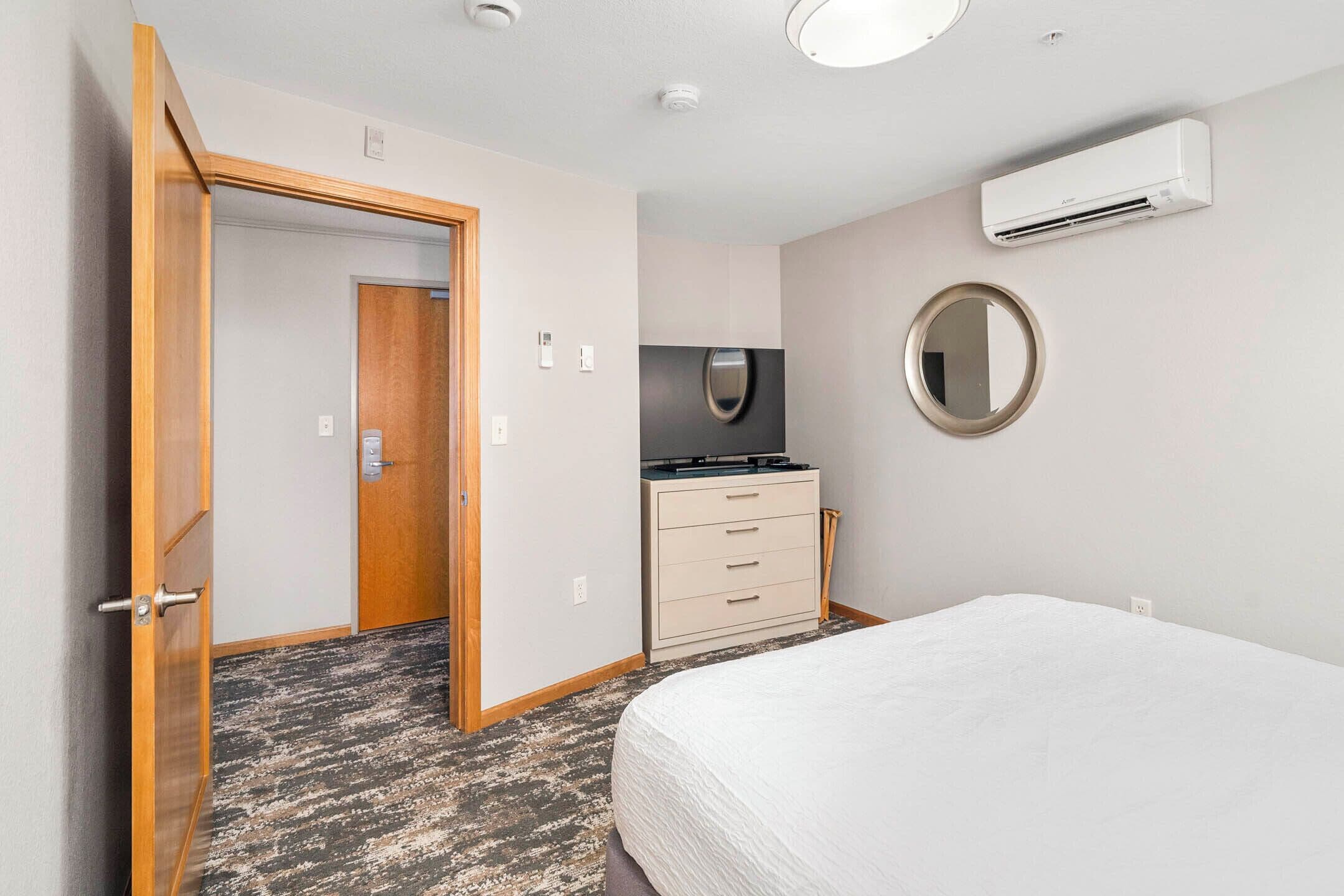 A hotel room with a bed, a dresser, a mirror, and an air conditioning unit.