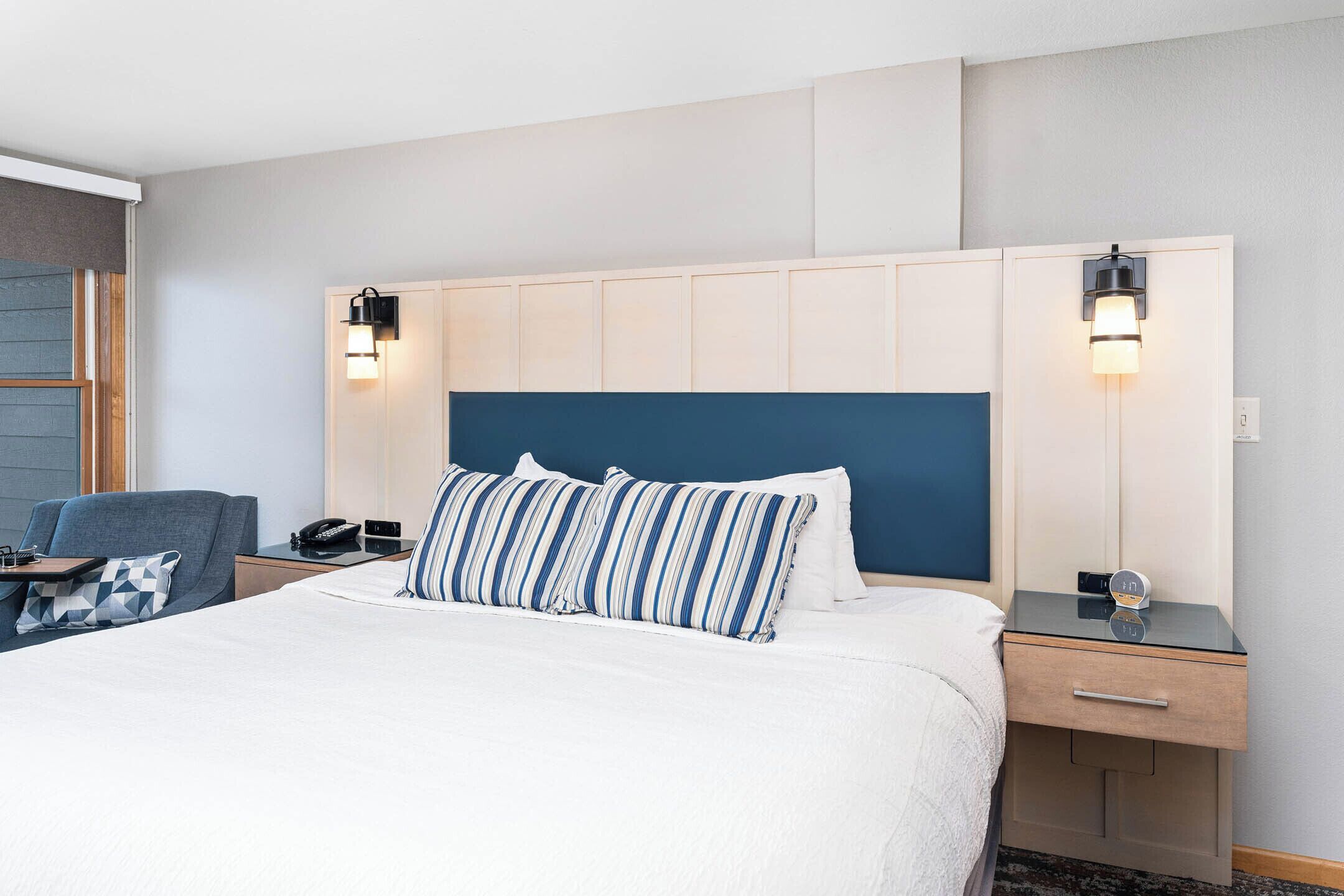 Een hotelkamer met een groot bed, een nachtkastje met een lamp, een stoel en een bureau met een telefoon.