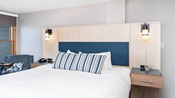 Een hotelkamer met een groot bed, een nachtkastje met een lamp, een stoel en een bureau met een telefoon.