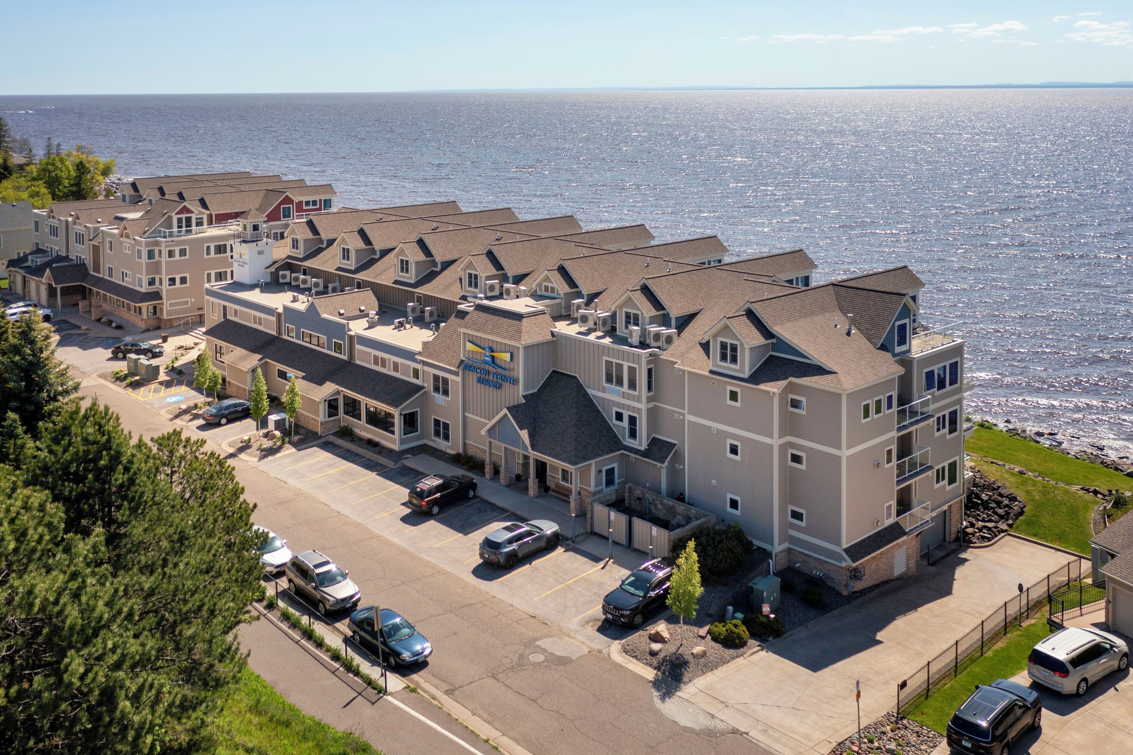 A coastal hotel with multiple buildings, a parking lot, and a view of the sea.