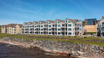 A row of multi-story buildings with balconies, situated by a rocky shoreline.