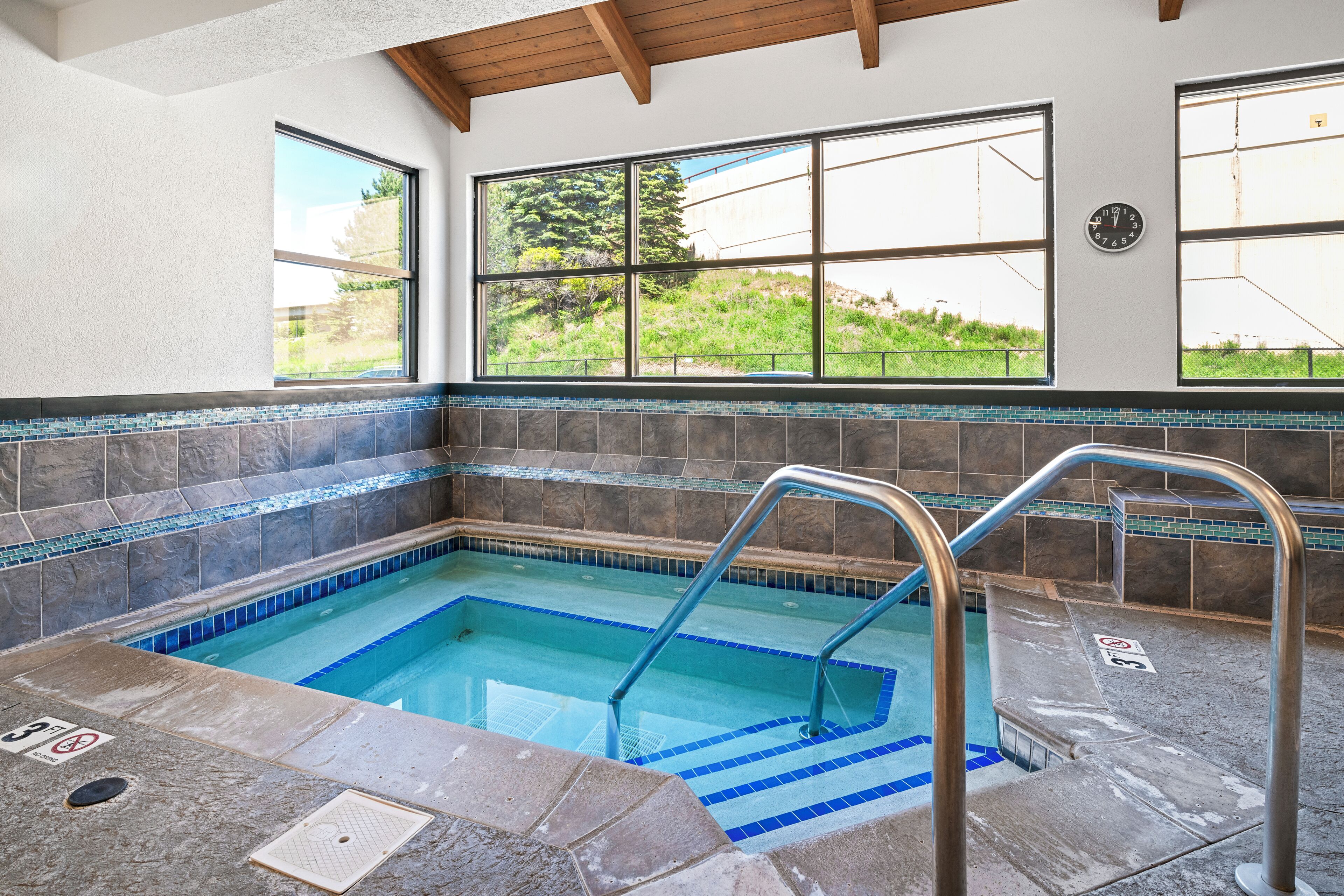 Une piscine à l’eau d’un bleu cristallin, entourée de dalles de pierre et bordée de carreaux.