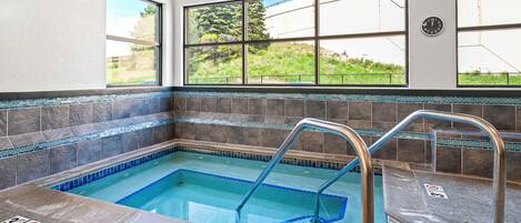 A swimming pool with clear blue water, surrounded by stone tiles and a tiled border.
