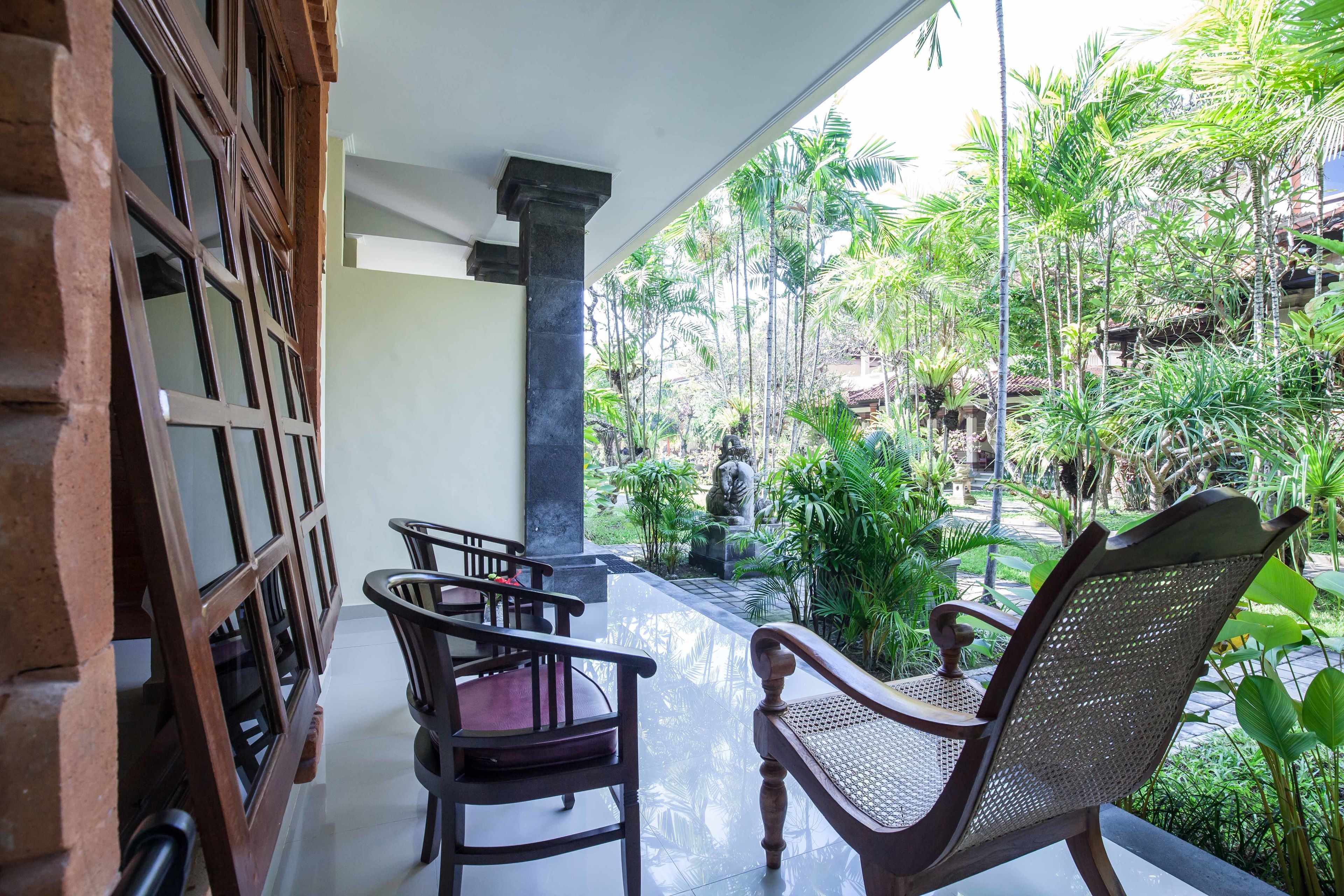 A covered patio with wooden furniture and a view of a lush garden.